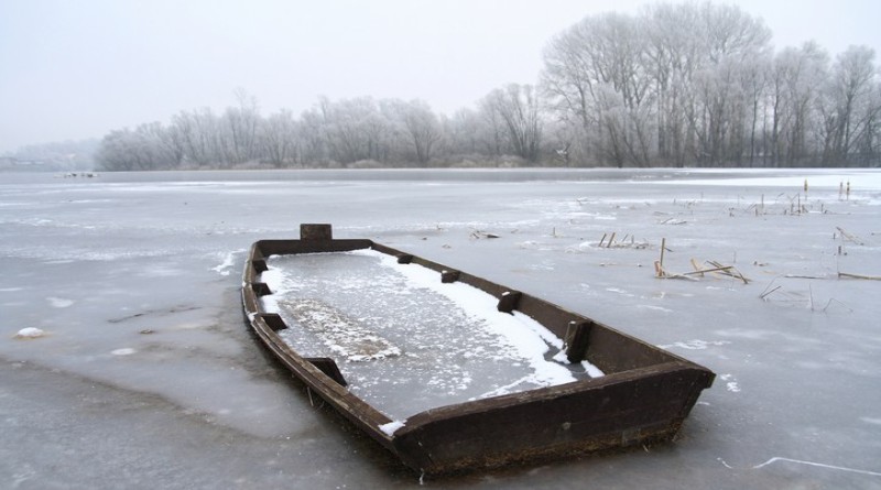 Winter landscape with wooden boat covered by ice on frozen lake